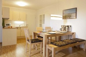 A compact kitchen with a microwave, sink, and a coffee maker. There is a dining table with chairs and a bench. - Holiday apartment in Norderney with Wi-Fi (Norderney)