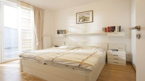 Un dormitorio con cama, mesitas de noche, una ventana con cortinas y una estantería con libros.