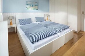 Een tweepersoonsbed met streepjesbeddengoed, een nachtkastje met lamp en een schilderij aan de muur.