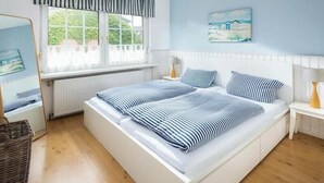 Un letto matrimoniale con lenzuola a righe, un comodino con una lampada, una finestra con tende e un quadro appeso al muro.
