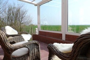 Een overdekt terras met rieten meubilair en uitzicht op een groen veld.