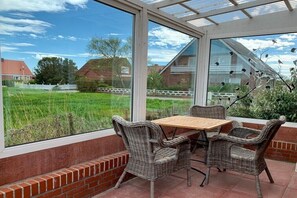 Eine überdachte Terrasse mit Korbmöbeln und Blick auf ein grünes Feld.