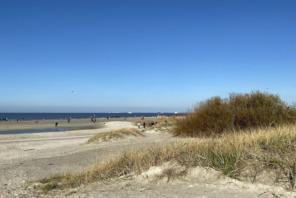 A beach with people walking and a clear sky.