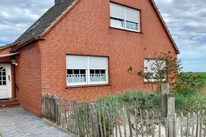 Een rode bakstenen woning met twee ramen, een houten hek en een verharde oprit.