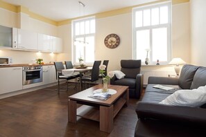 A modern living room with a sofa, a coffee table, and a dining area with chairs. - Friedrichstr. 36 Apt. 7 (Norderney)