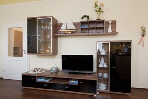 A living room with a flat-screen TV, wooden entertainment unit, glass cabinet, and decorative items. - Friedrichstr. 36 Apt. 7 (Norderney)
