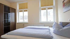 Ein Schlafzimmer mit einem Bett, einem Kleiderschrank und zwei Fenstern mit Jalousien.
