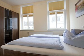 Un dormitorio con una cama, un armario y dos ventanas con persianas.