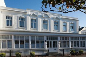 Un edificio blanco con múltiples ventanas y una puerta, rodeado por una cerca de metal negro.