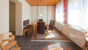 Ein Essbereich mit Holzboden, einem Tisch mit Stühlen, einem gemusterten Teppich und einem Fenster mit roten Vorhängen.