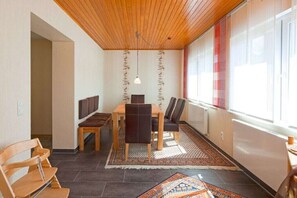 A dining area with a wooden ceiling, a table with chairs, a patterned rug, and a window with red curtains. - Holiday home in Norderney with Wi-Fi (Norderney)