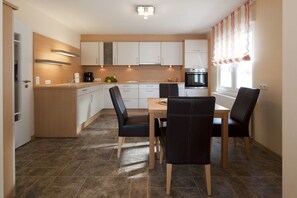 A modern kitchen with white cabinets, a dining table with chairs, and a built-in oven. - Holiday home in Norderney with Wi-Fi (Norderney)