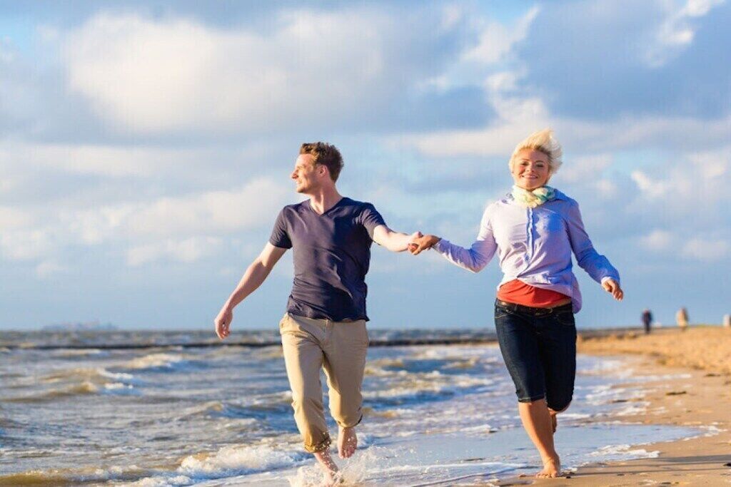 Deux personnes se promènent sur une plage, avec l’océan en arrière-plan.