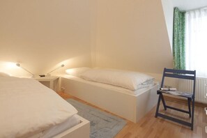 Un dormitorio con cama, mesita de noche, lámpara, silla y una ventana con cortinas.