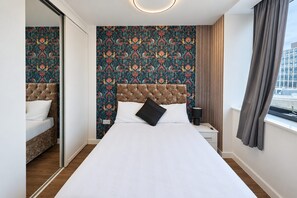 Ein Hotelzimmer mit Bett, Nachttisch, Spiegel und einem Fenster mit Vorhängen.