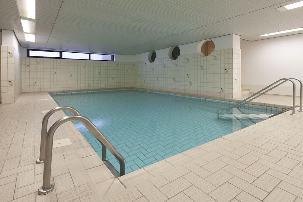Ein Hallenbad mit gefliesten Wänden und blauem Wasser.