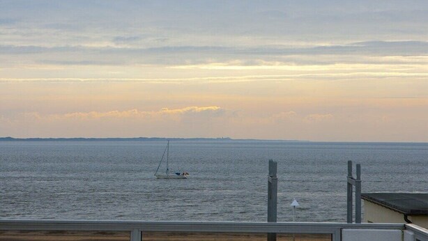 Une vue sur une mer calme, avec un voilier et une côte lointaine.