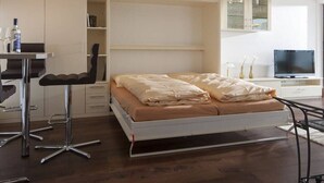 Une chambre à coucher comprenant un lit, un bureau avec une chaise, un téléviseur et des étagères intégrées.