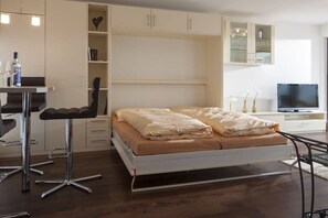 Un dormitorio con cama, un escritorio con silla, televisor y estanterías empotradas.