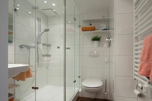 Un baño moderno con ducha de vidrio, lavamanos blanco, inodoro y toallero.