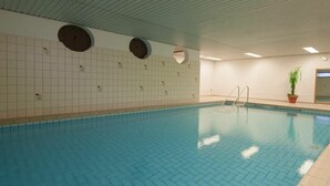 Une piscine intérieure avec un sol carrelé, une échelle et une plante en pot.