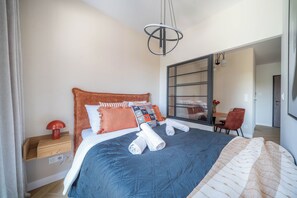 A neatly made bed with a blue quilt, a red lamp, and a wooden nightstand. - Kierbedzia Comfort Stay, Mokotów, Warsaw (Warszawa)