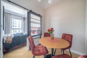 A modern interior with a dining area featuring a round table and red chairs, a sofa with a blanket, and a view through a large window. - Kierbedzia Comfort Stay, Mokotów, Warsaw (Warszawa)