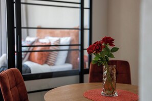 A room with a round table, a vase with red flowers, and a view of a bed with pillows through a window. - Kierbedzia Comfort Stay, Mokotów, Warsaw (Warszawa)
