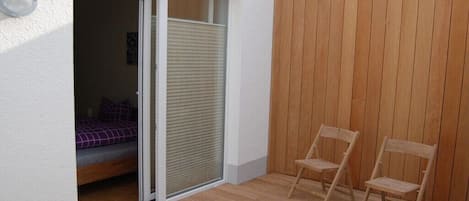 A room with a bed, a sliding door, and two wooden chairs.