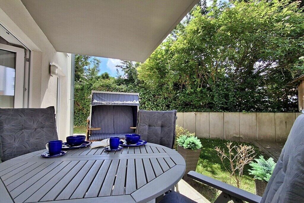 A round table with blue cups and saucers, a barbecue grill, and a view of a garden with a wooden fence.