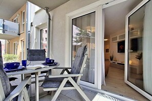 Een balkon met een tafel voor twee, een stoel en een glazen schuifdeur die leidt naar een binnenruimte.