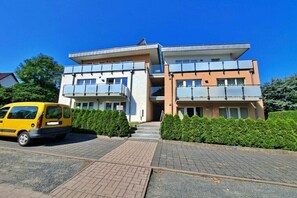 A multi-story building with a parking area and a yellow van parked in front. - Villa Bettina Apartment 03 (Heringsdorf (Seebad))