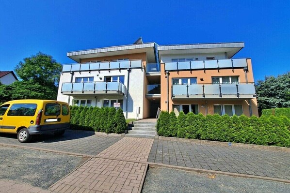 Een meerlaags gebouw met een parkeerplaats en een gele bestelwagen ervoor geparkeerd.