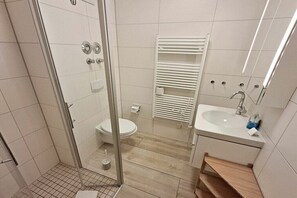 Een moderne badkamer met een douche met glazen wand, een toilet, een wastafel en een handdoekhouder.