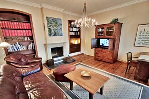 Ein Wohnzimmer mit einer Ledersofa, einem Holztisch, einem Kamin, Bücherregalen und einem Fernseher.