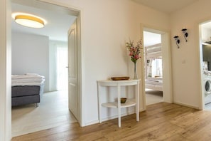 A modern interior with a wooden floor, a white wall, a small white table with a vase of flowers, and a grey sofa. - Holiday apartment F5 (Graal-Müritz)