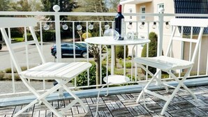 Un balcon avec une table et deux chaises, une bouteille de vin et une guirlande lumineuse.