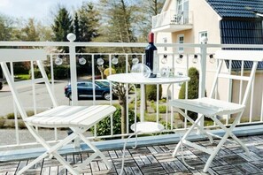 Een balkon met een tafel en twee stoelen, een fles wijn en een lichtslingering.