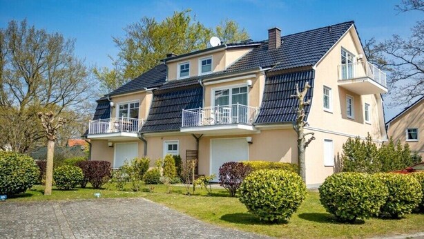 Un immeuble résidentiel à deux étages, doté d’un toit en pente, d’un balcon à l’étage supérieur et d’un garage.