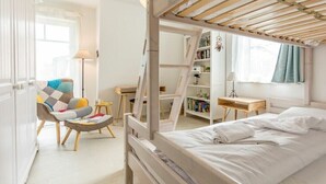 Une chambre avec un lit superposé, une chaise dotée d’un coussin coloré, une table de chevet, une bibliothèque et une fenêtre avec des rideaux.