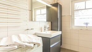 Une salle de bain moderne équipée d’un lave-linge Bosch, d’un lavabo et d’un miroir placé au-dessus.