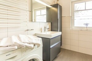 Een moderne badkamer met een Bosch wasmachine, een wastafel en een spiegel erboven.