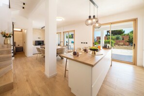 Una cocina moderna con una isla central, un área de comedor con sillas y vistas al exterior a través de amplios ventanales correderas.