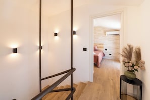 Ein modernes Hotelzimmer mit einer Holztreppe, einem Bett mit rosa Decke und einer Vase mit getrockneten Blumen.