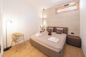Un dormitorio con una cama, mesitas de noche, una silla y una lámpara de pie.