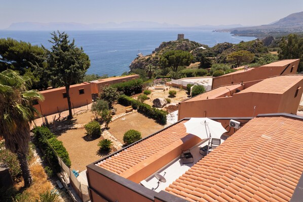 Un barrio residencial con edificios de tejados de terracota, vistas despejadas al mar y una colina rocosa al fondo.