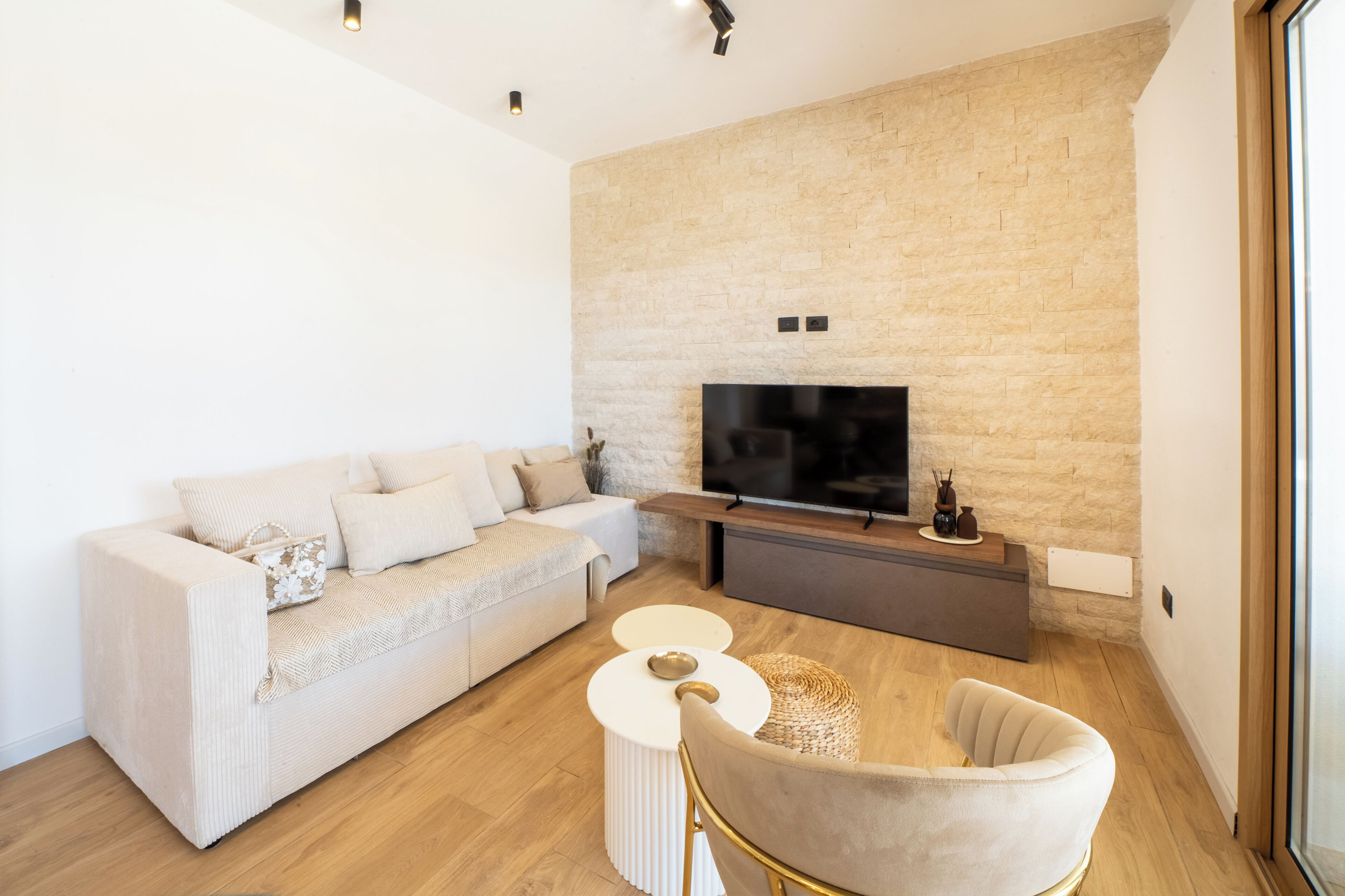 Una sala de estar moderna con un sofá, un televisor montado en una pared de piedra y una mesa redonda de centro.