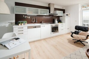 A modern kitchen with white cabinetry, a built-in oven, and a dining area with a white table and a black chair. - Holiday apartment in Norderney with Wi-Fi (Norderney)