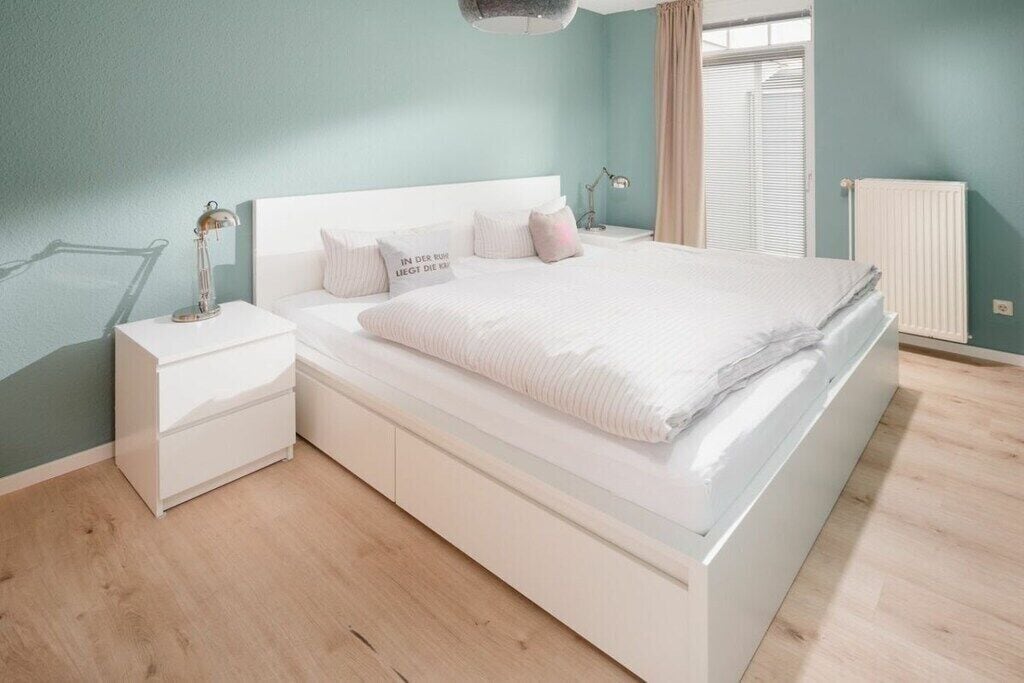 Une chambre à coucher moderne avec un lit blanc, des tables de chevet et une fenêtre avec des stores.