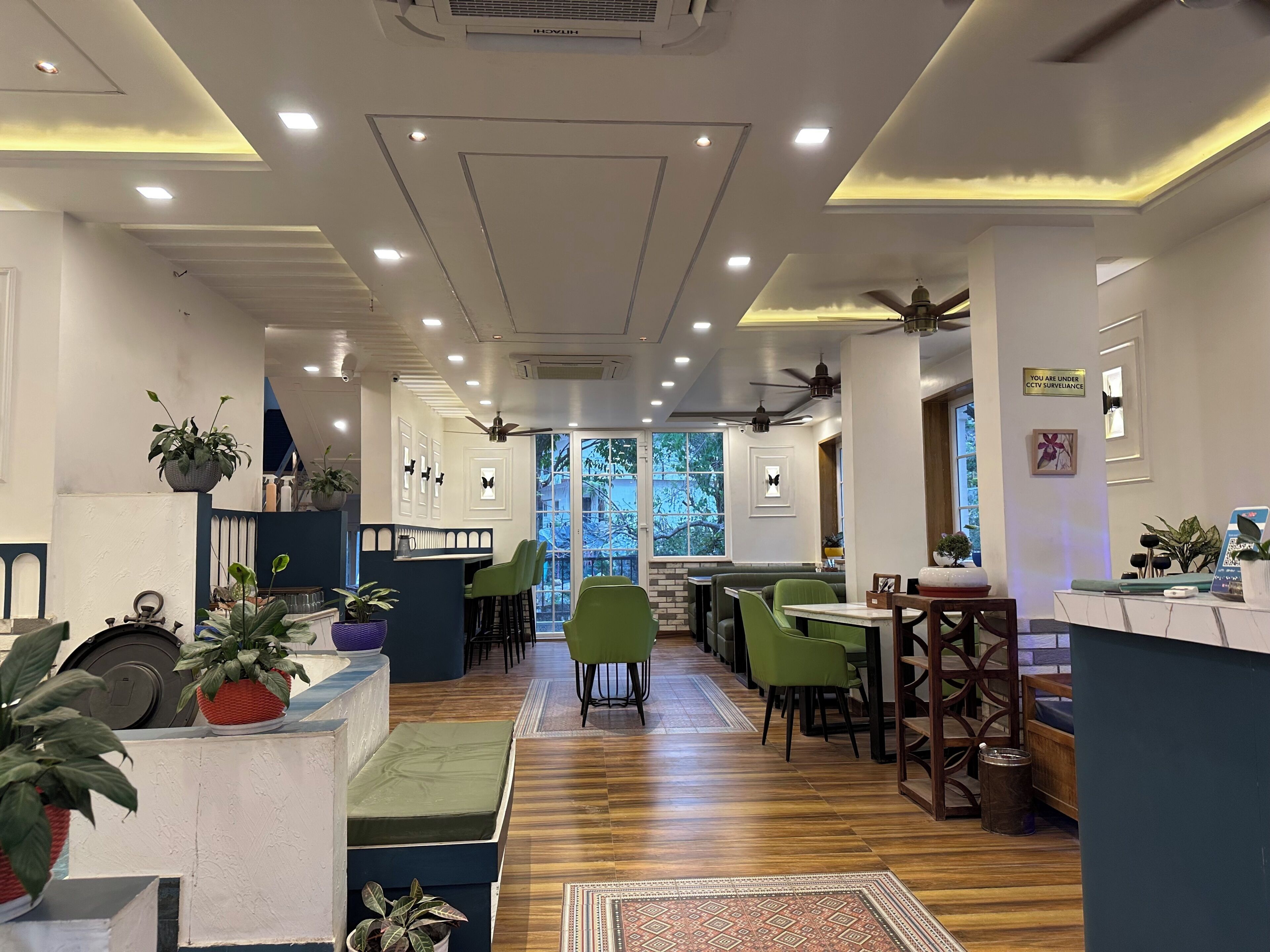 Un interior de restaurante con una barra larga, sillas verdes y plantas en macetas.